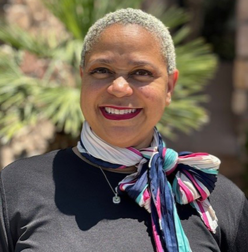 Professional woman smiling outdoors wearing colorful scarf and dark shirt, dental office portrait.