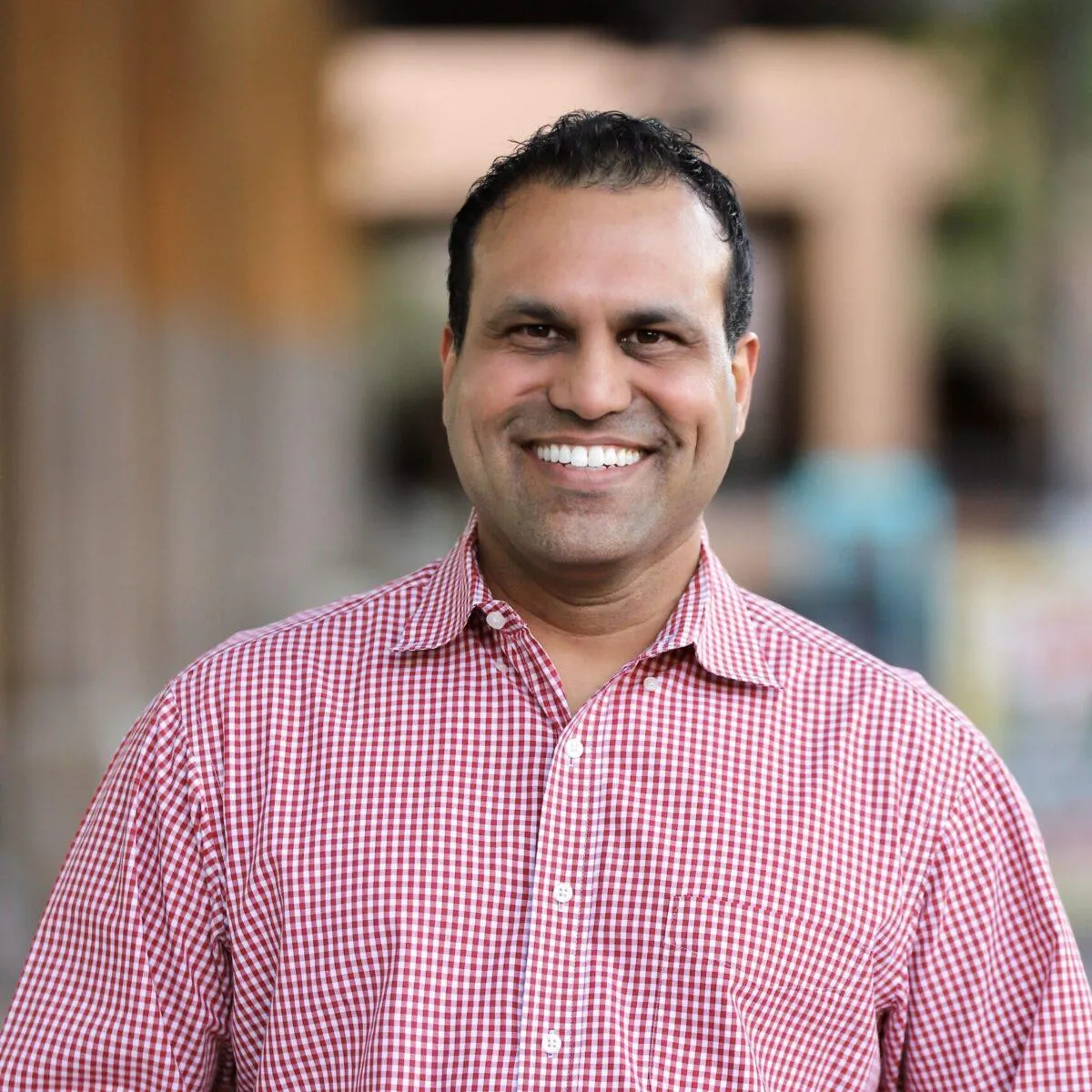 Professional man in red checkered shirt smiling outdoors, dental practice portrait.
